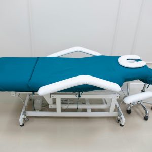 A sterile and adjustable medical examination table with a teal mattress in a clinical setting.